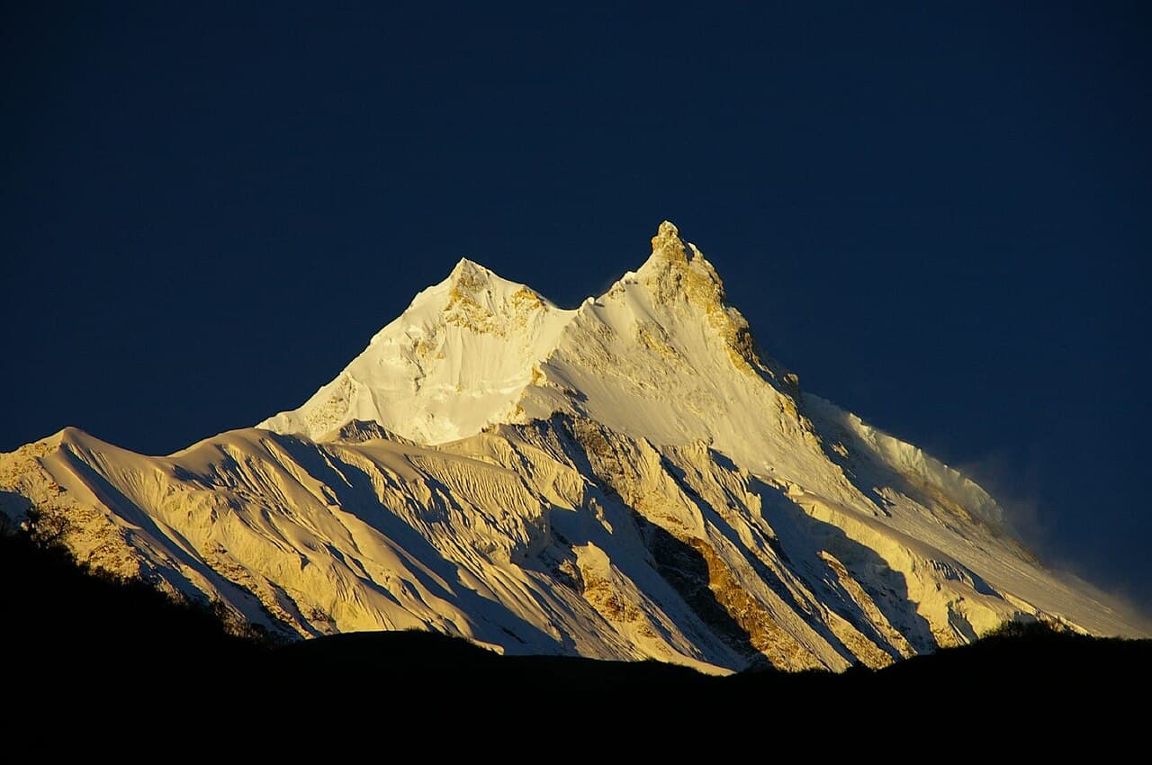 Manaslu at sunrise, its twin summits lit gold above a dark ridge